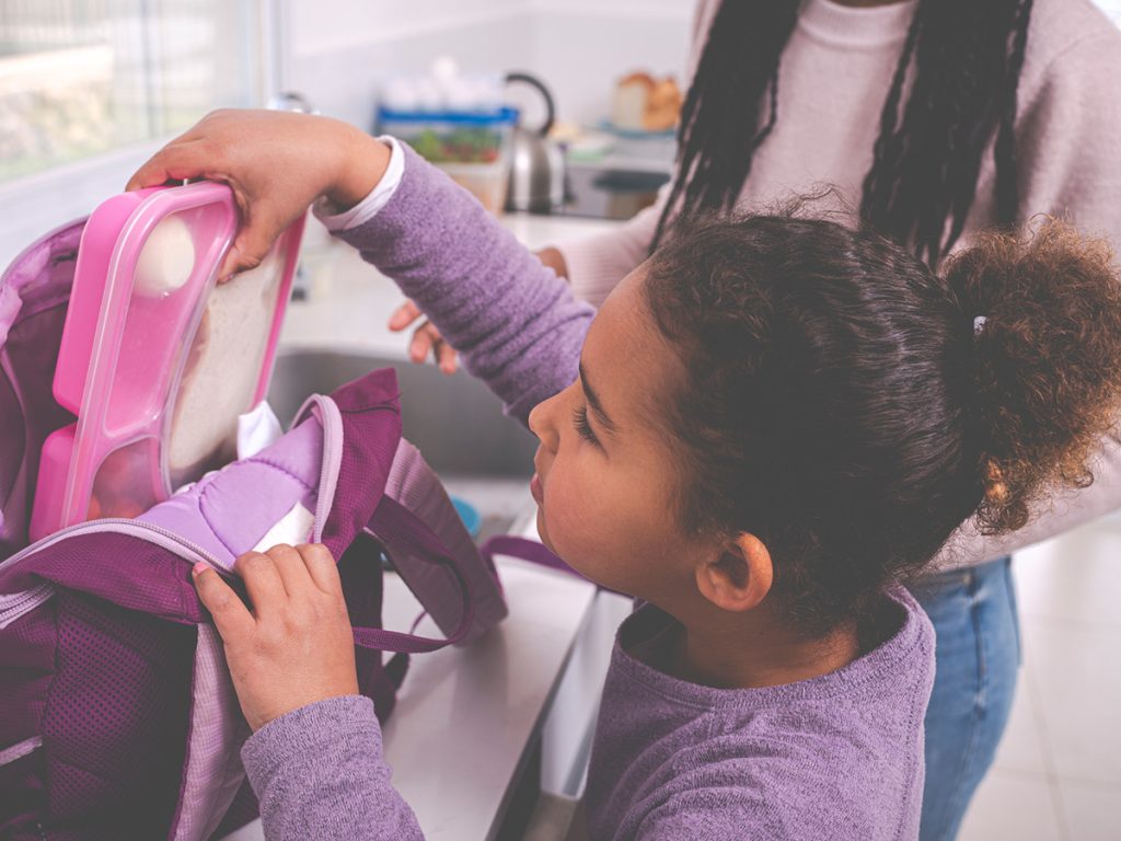 Girl packing bento box lunch into backpack